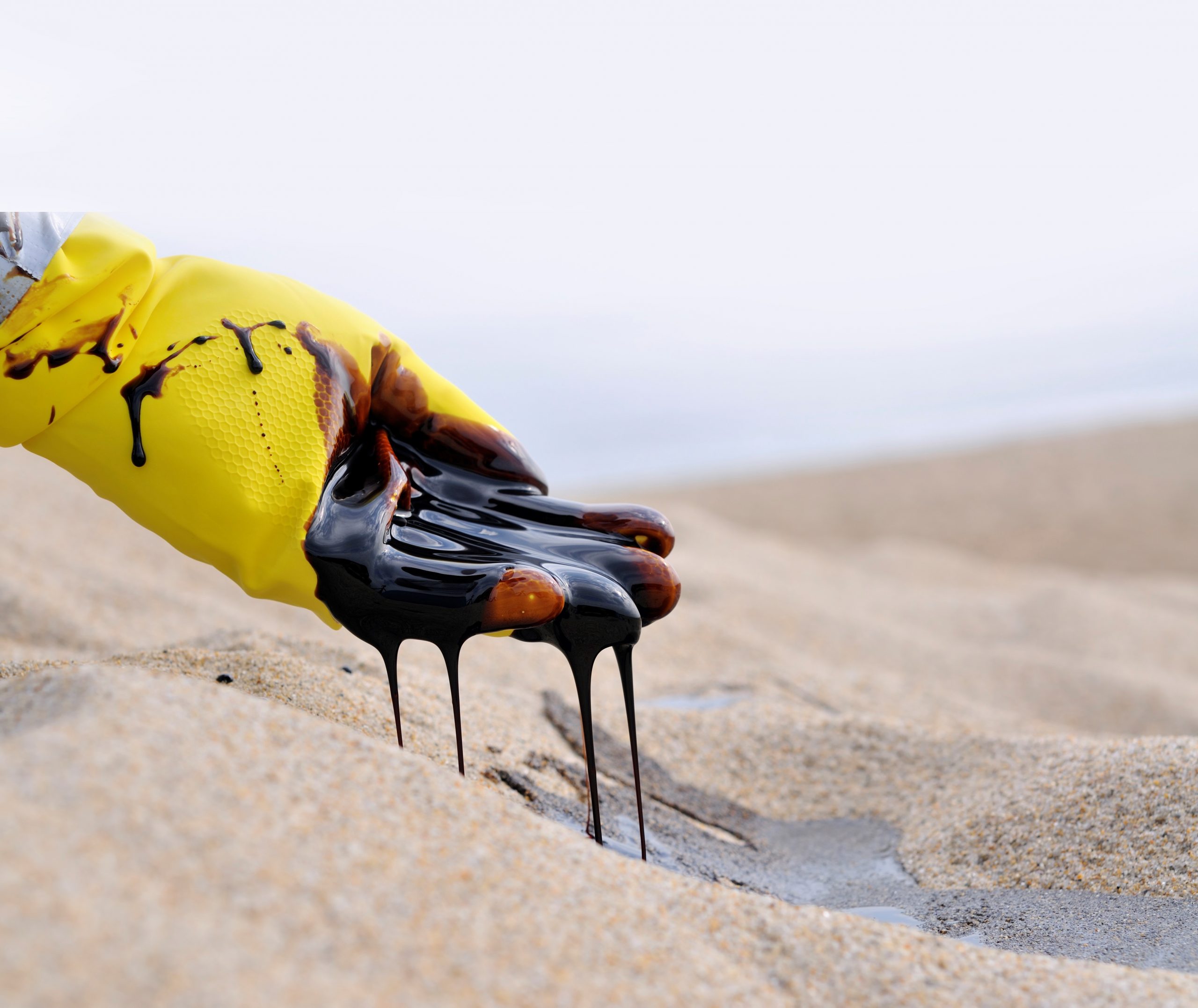 A yellow glove holding a handful of oil over sand