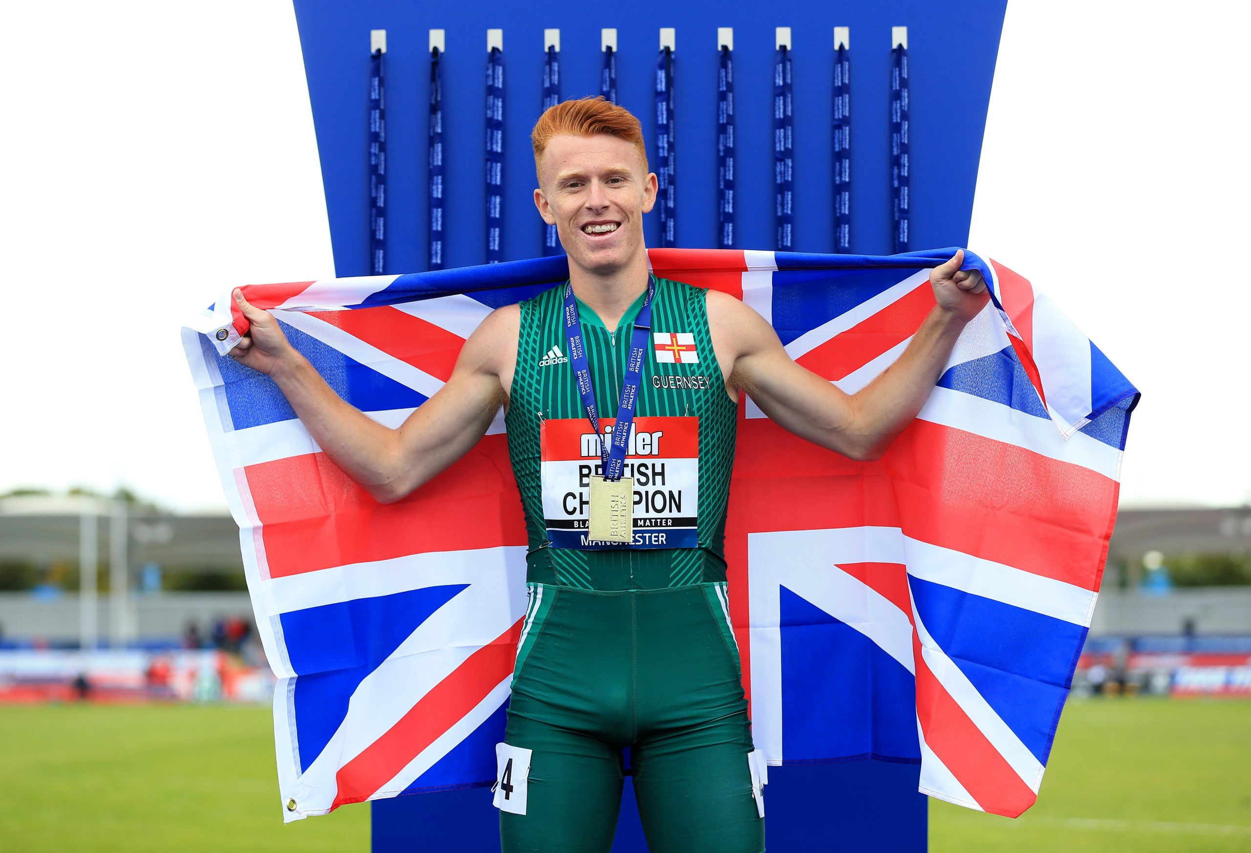 Alastair Chalmers posing at the CommonWealth Games while holding up a GB flag